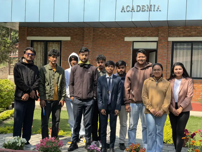 Group of eleven people standing together outside the brick Academia College building.