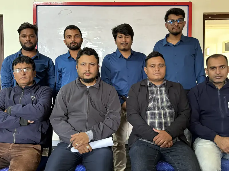 Group portrait of eight people in front of a whiteboard, four seated and four standing behind them.